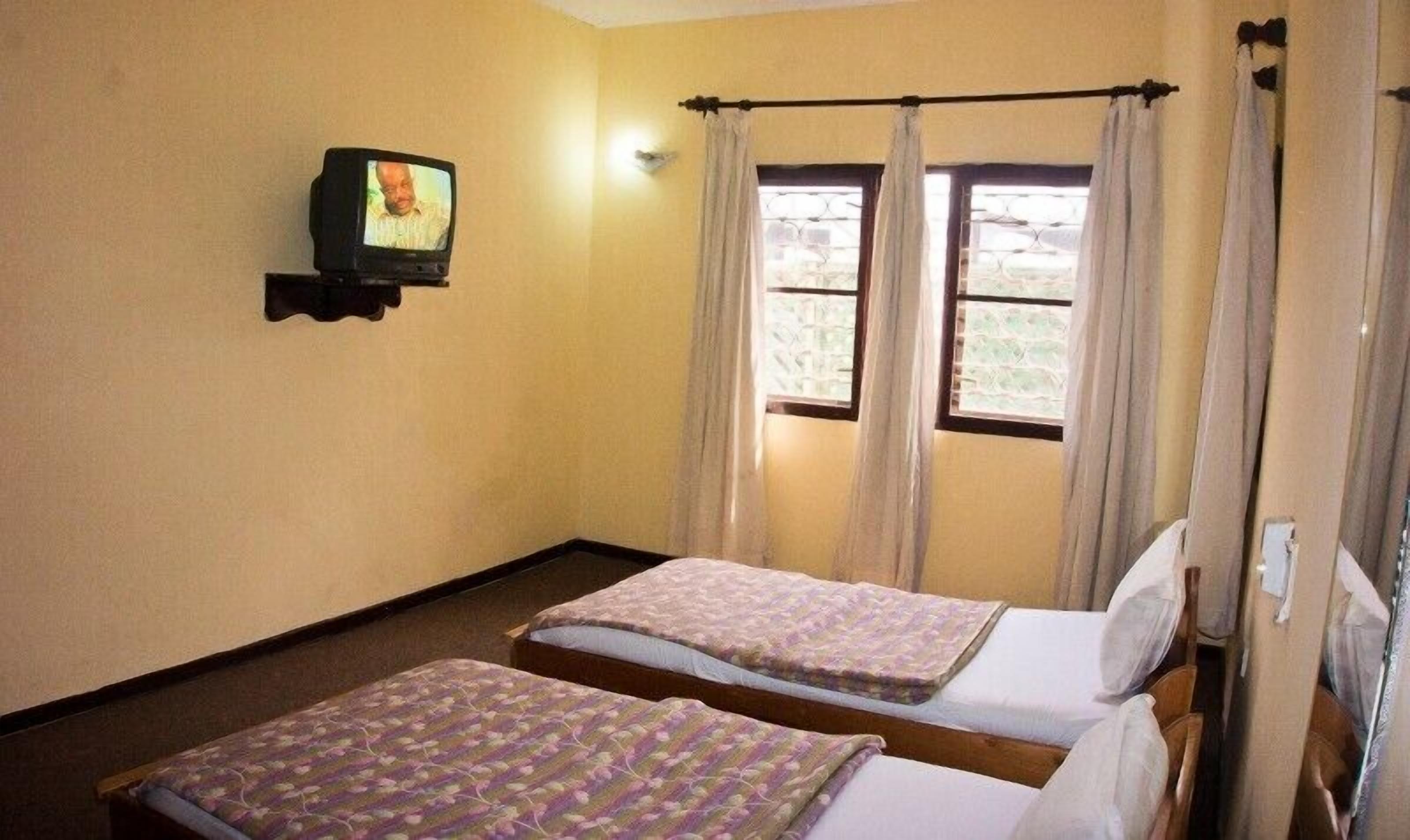 A room with two beds, a television on the wall, and a window with curtains.