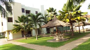 A courtyard with palm trees, a thatched-roof gazebo, and a building with a white facade. - Pekan Hotel (Accra)