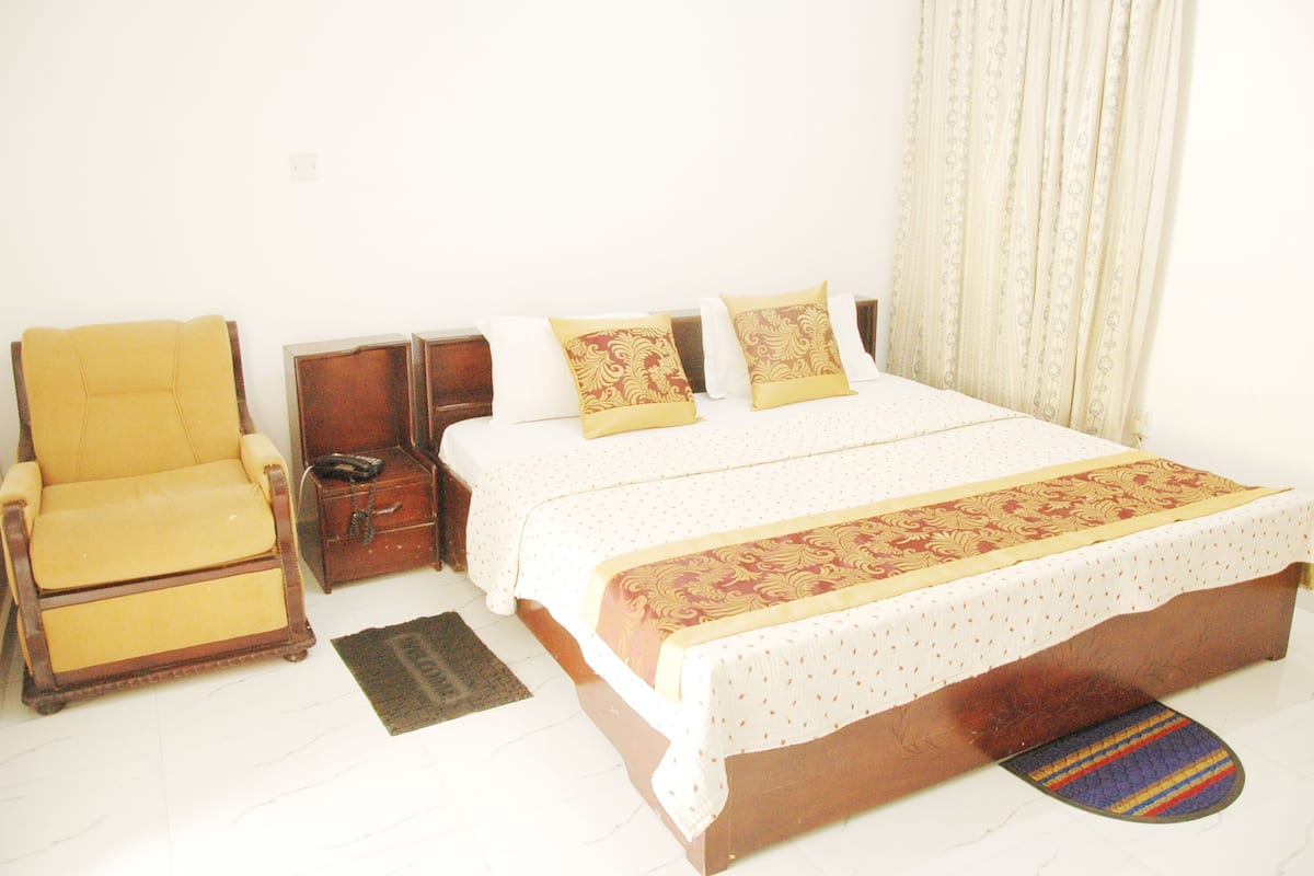 A hotel room with a bed, a chair, a nightstand, and a rug.