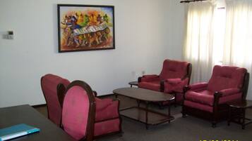 A room with a desk, two armchairs, a coffee table, and a painting on the wall.