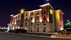 Un hotel de varios pisos con un llamativo letrero 'My Place', un estacionamiento y una fachada bien iluminada.