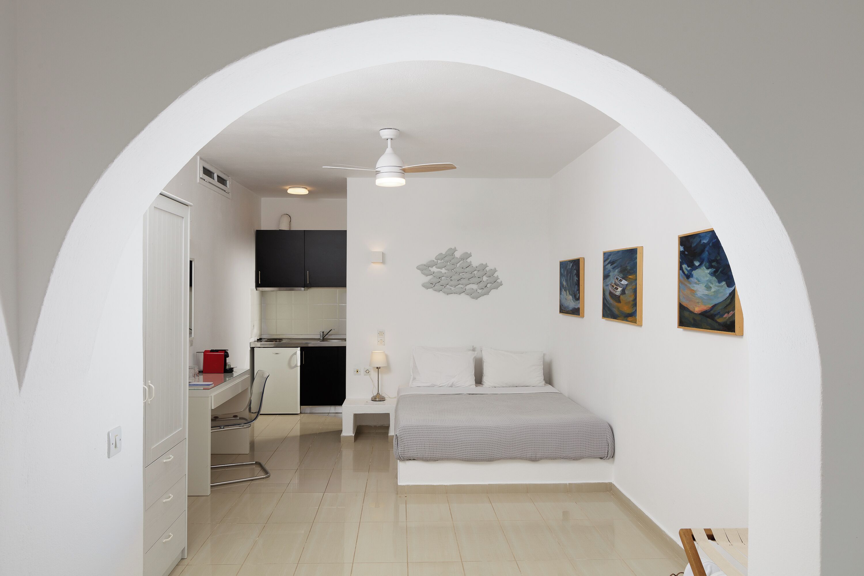 A bedroom with a bed, a desk, and a kitchenette.