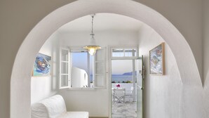 Ein weiß gestrichener Raum mit einem weißen Sofa, einem Fenster mit geöffneten Läden und Blick aufs Meer.