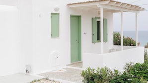 Ein weißes Gebäude mit grünen Türen und Fensterläden, einer kleinen Veranda und Blick auf das Meer.