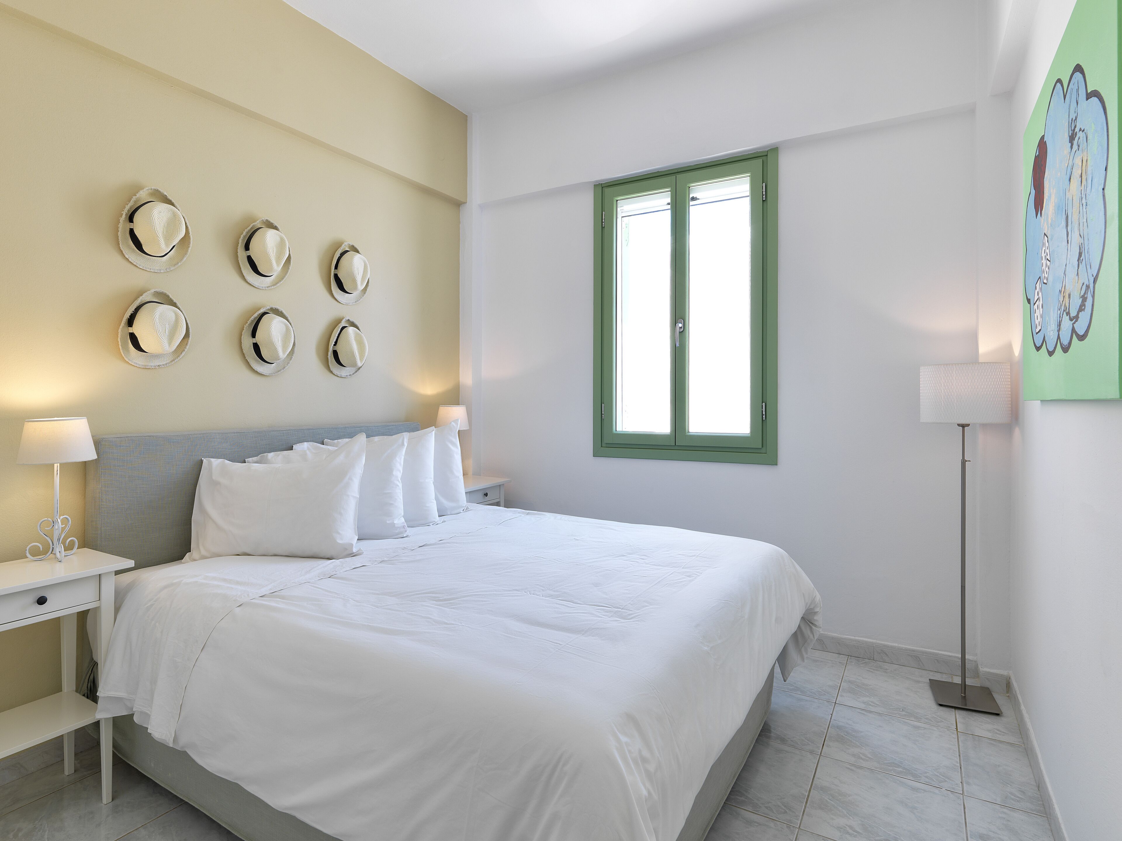 Quarto com cama, mesas de cabeceira, janela e decorações nas paredes.