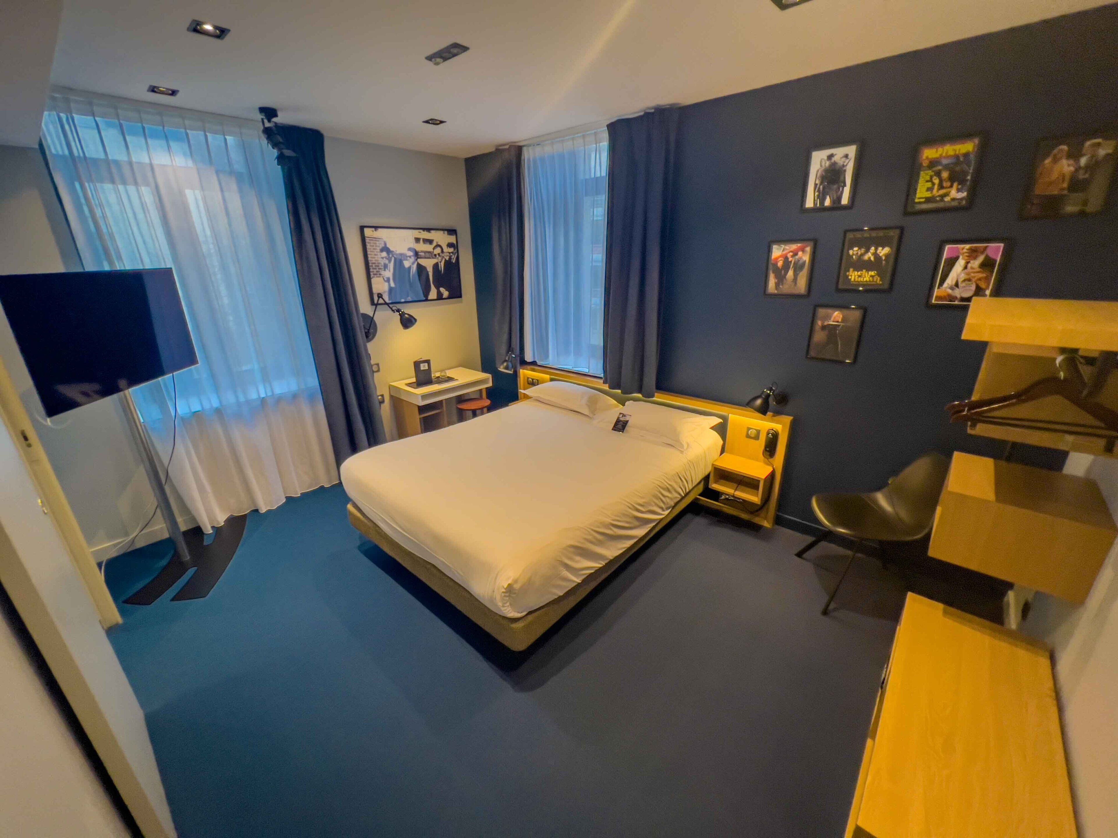 A hotel room with a bed, a desk, a chair, a TV, and a wardrobe.