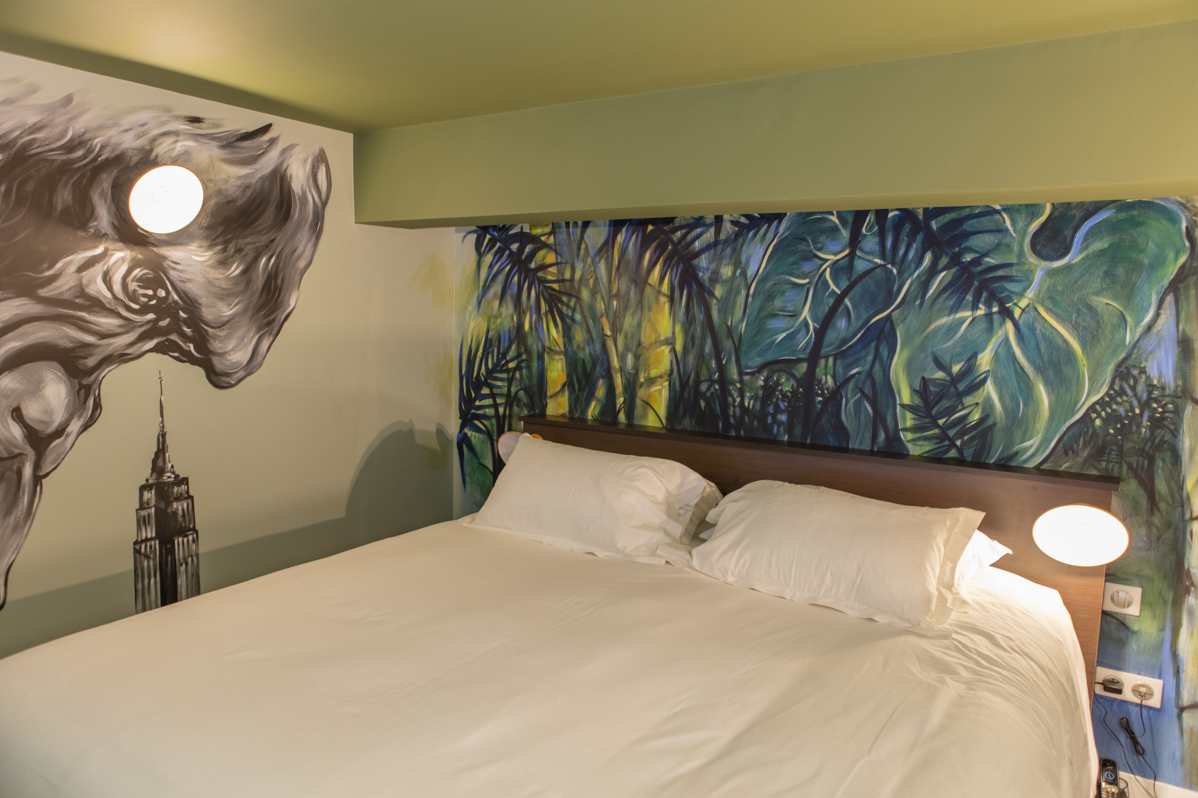 A hotel room with a large bed, a mural of a horse and the Empire State Building, and a tropical leaf pattern on the wall.