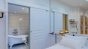 A modern bedroom with a large bed, a white bathtub, and a mirror reflecting the room.