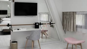 Habitación de hotel moderna con un espejo grande, un televisor de pantalla plana, un escritorio pequeño, una silla, un taburete rosa y una ventana con cortinas.