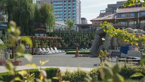 A hotel courtyard with lounge chairs, a rock formation, and a pergola. - DAS Club Hotel Sunny Beach (Nessebar)