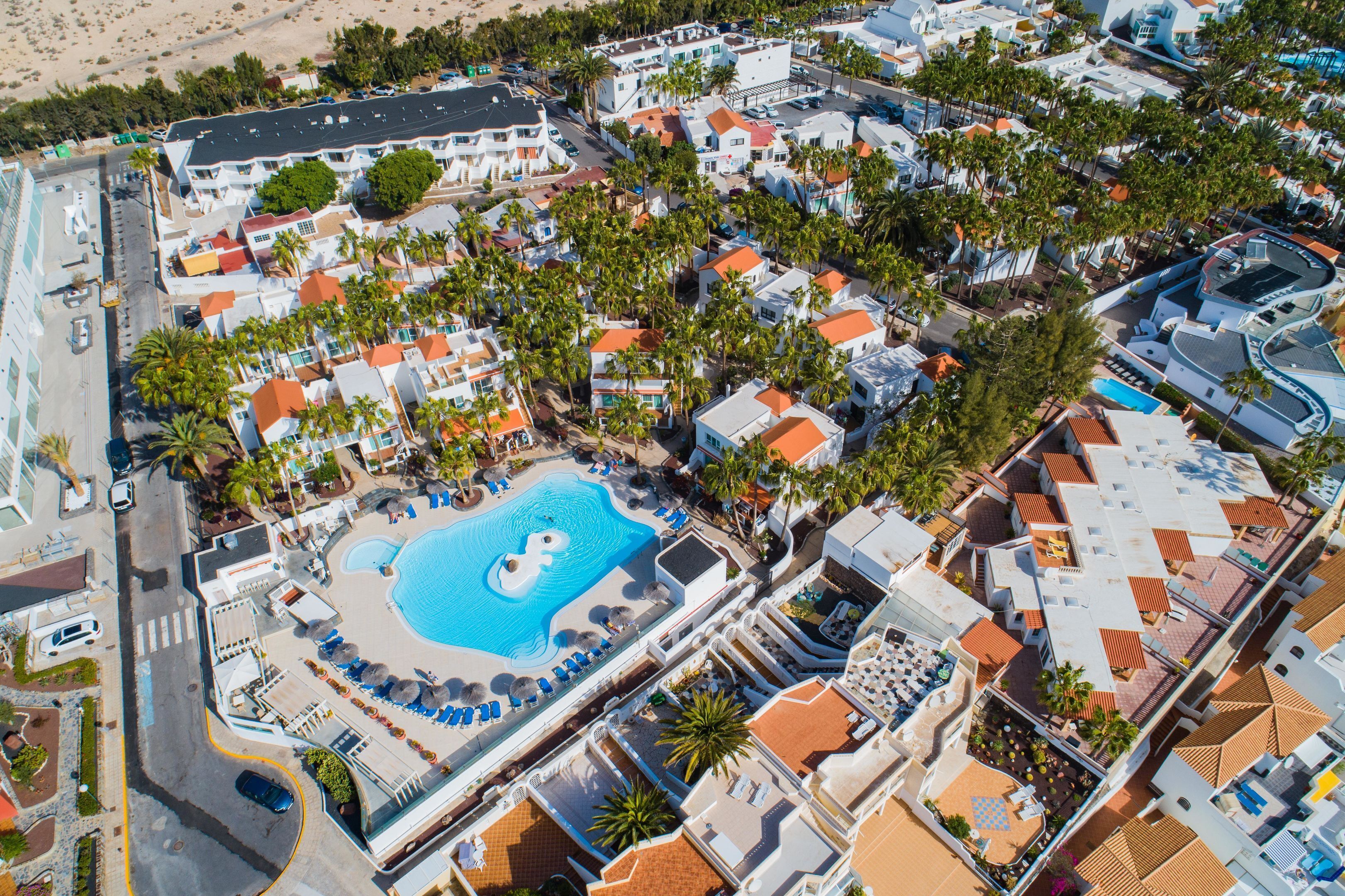 Vista aérea de un resort con una piscina central rodeada de sillones de descanso y palmeras.