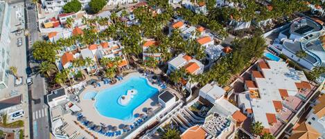 Vista aérea de un resort con una piscina central rodeada de sillones de descanso y palmeras.