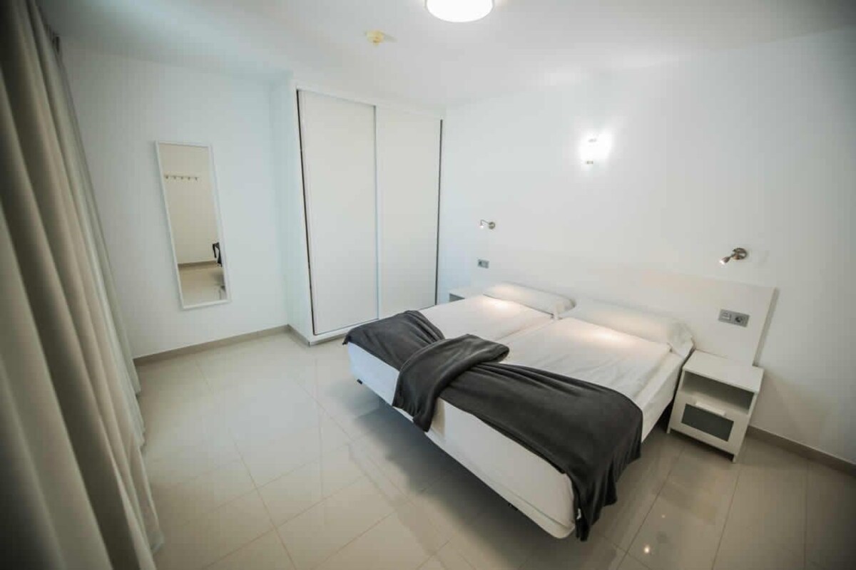 Un dormitorio moderno y bien iluminado, con cama, mesitas de noche, armario y espejo.
