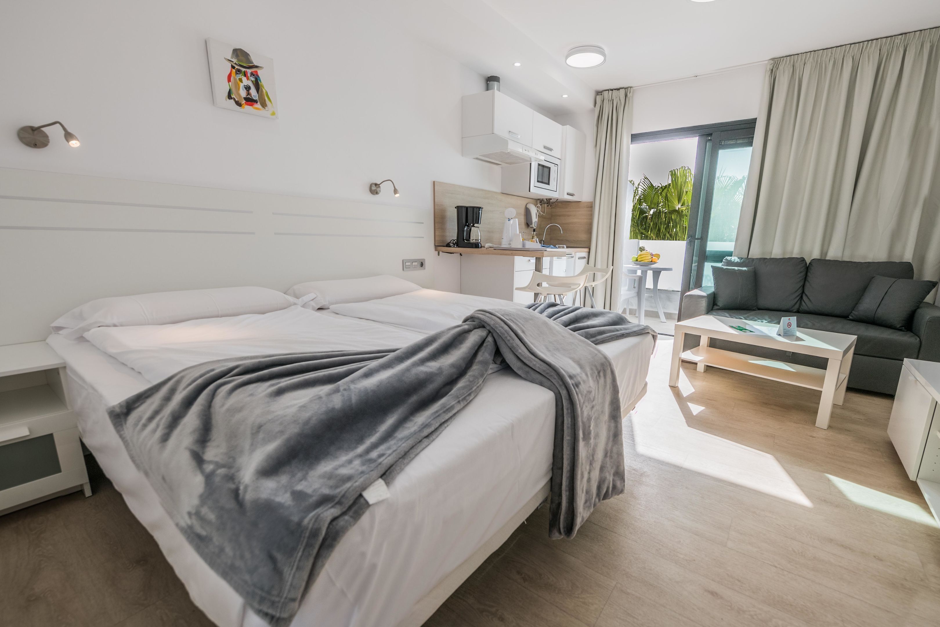 Una habitación de hotel moderna con una cama grande, kitchenette, zona de estar y vistas al exterior.