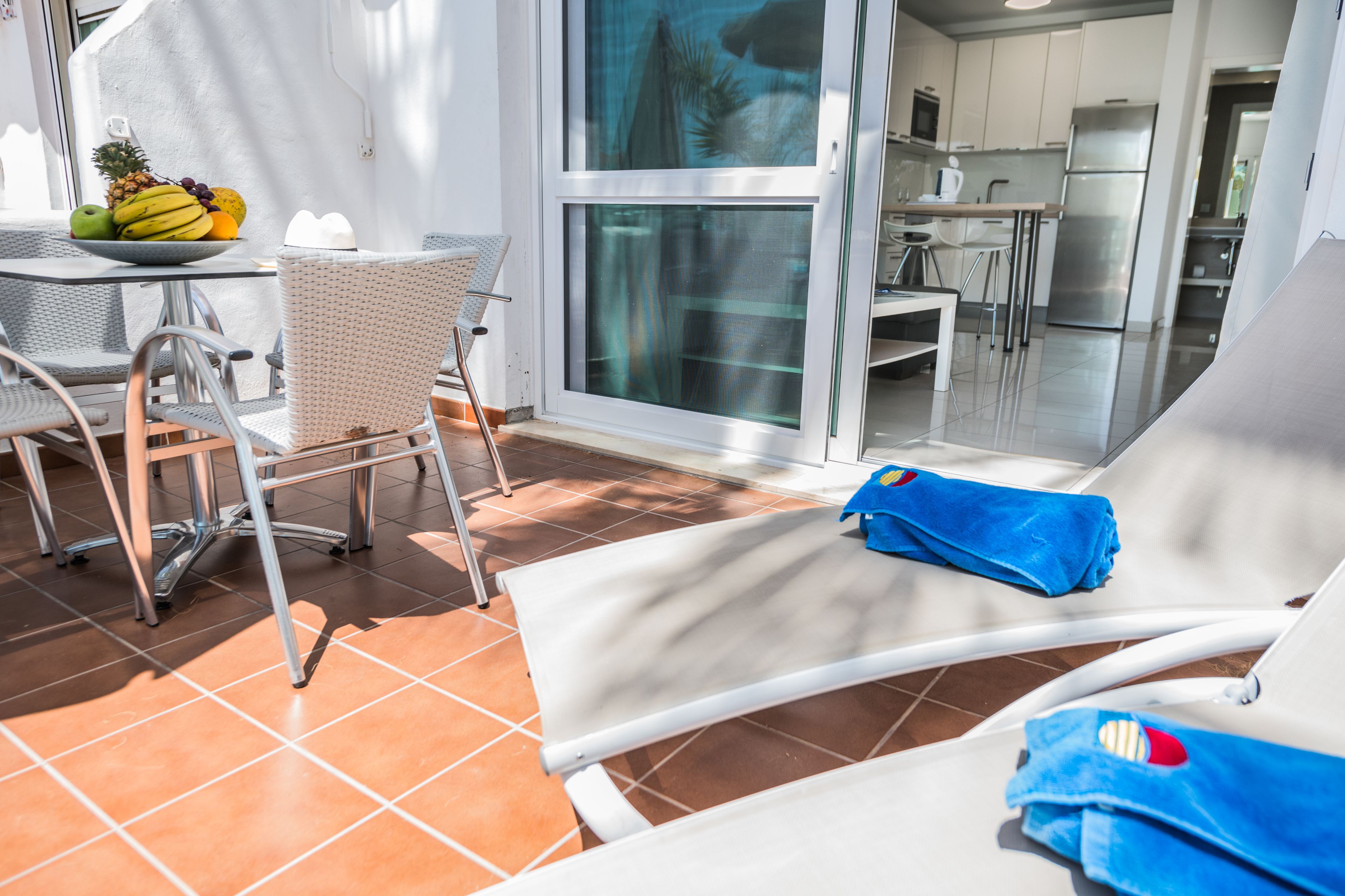 A sunlit outdoor seating area with a table, chairs, and a fruit bowl.