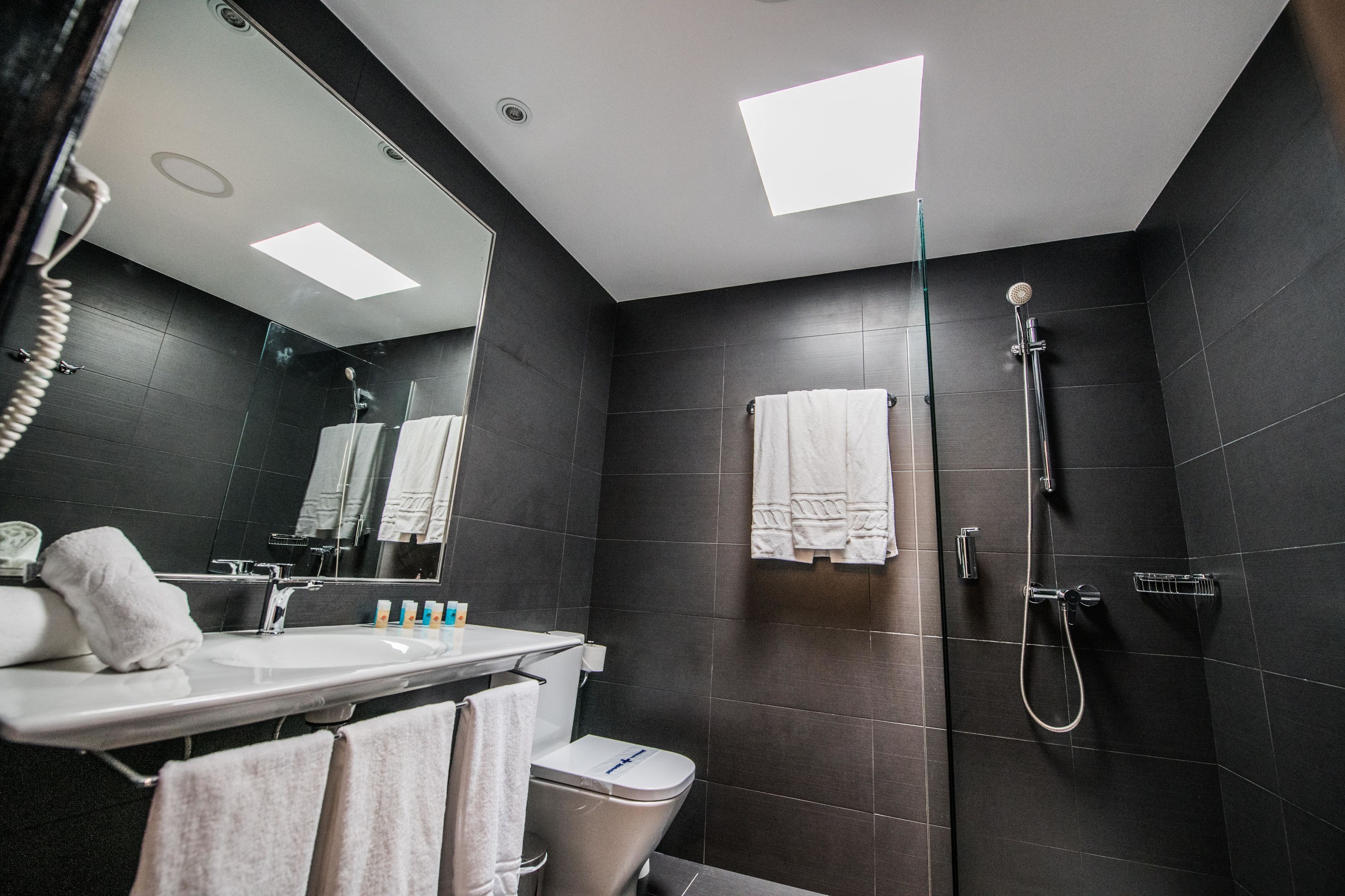 A modern bathroom with a large mirror, a sink, a toilet, and a shower area.