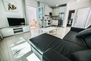 Una sala de estar moderna con un sofá negro, un televisor de pantalla plana y un ventanal que da a un comedor.