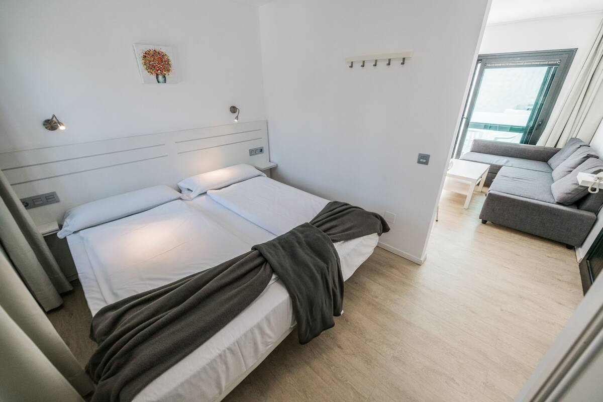 A modern bedroom with a bed, bedside tables, a small table, and a sofa.