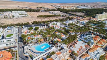 Vue aérienne d’une station balnéaire dotée d’une piscine centrale, de plusieurs bâtiments et d’une plage.
