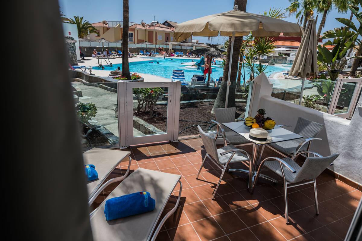 A poolside area with a table, chairs, and umbrellas.