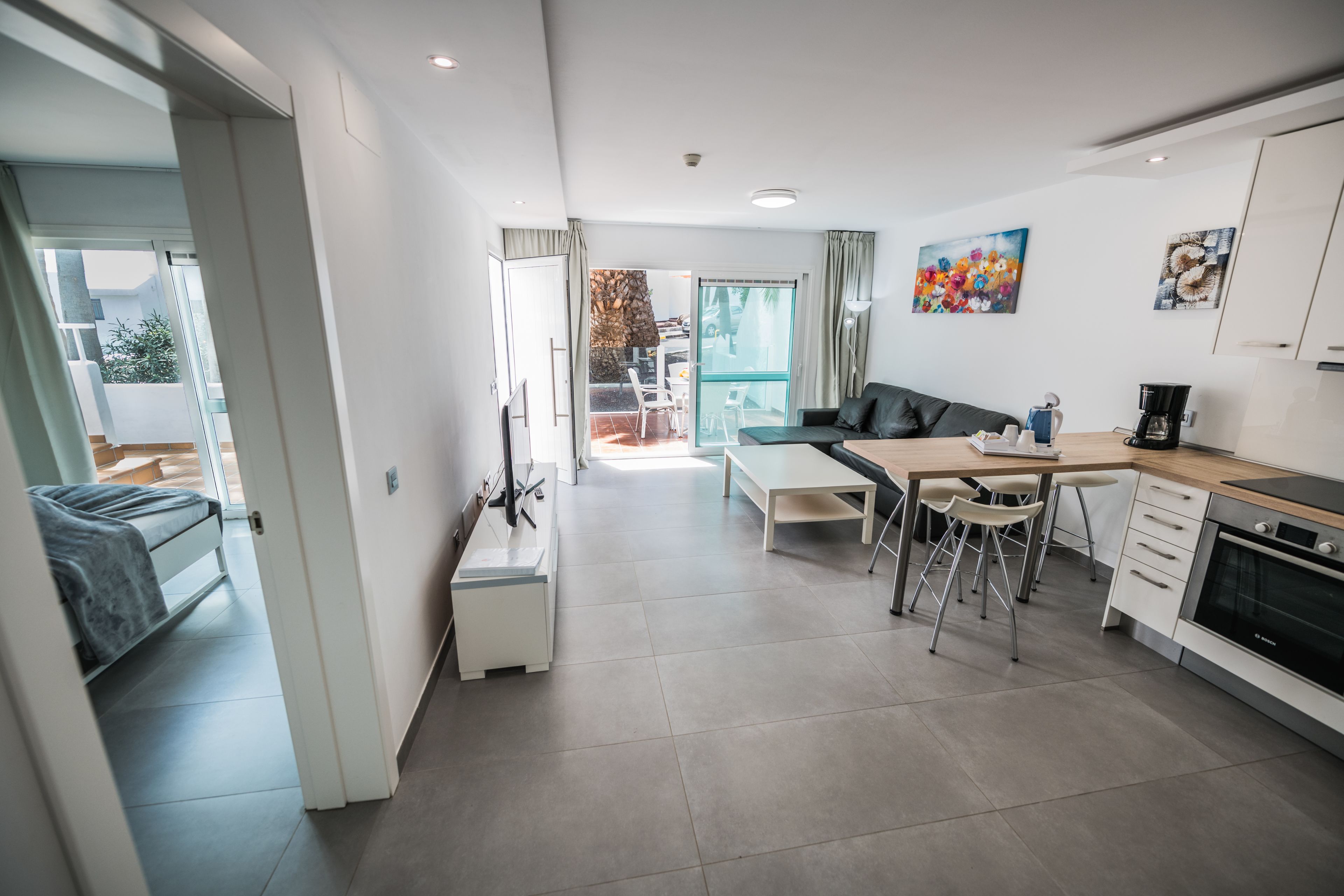 A modern kitchen with a dining area, a sofa, and a view of the outside.