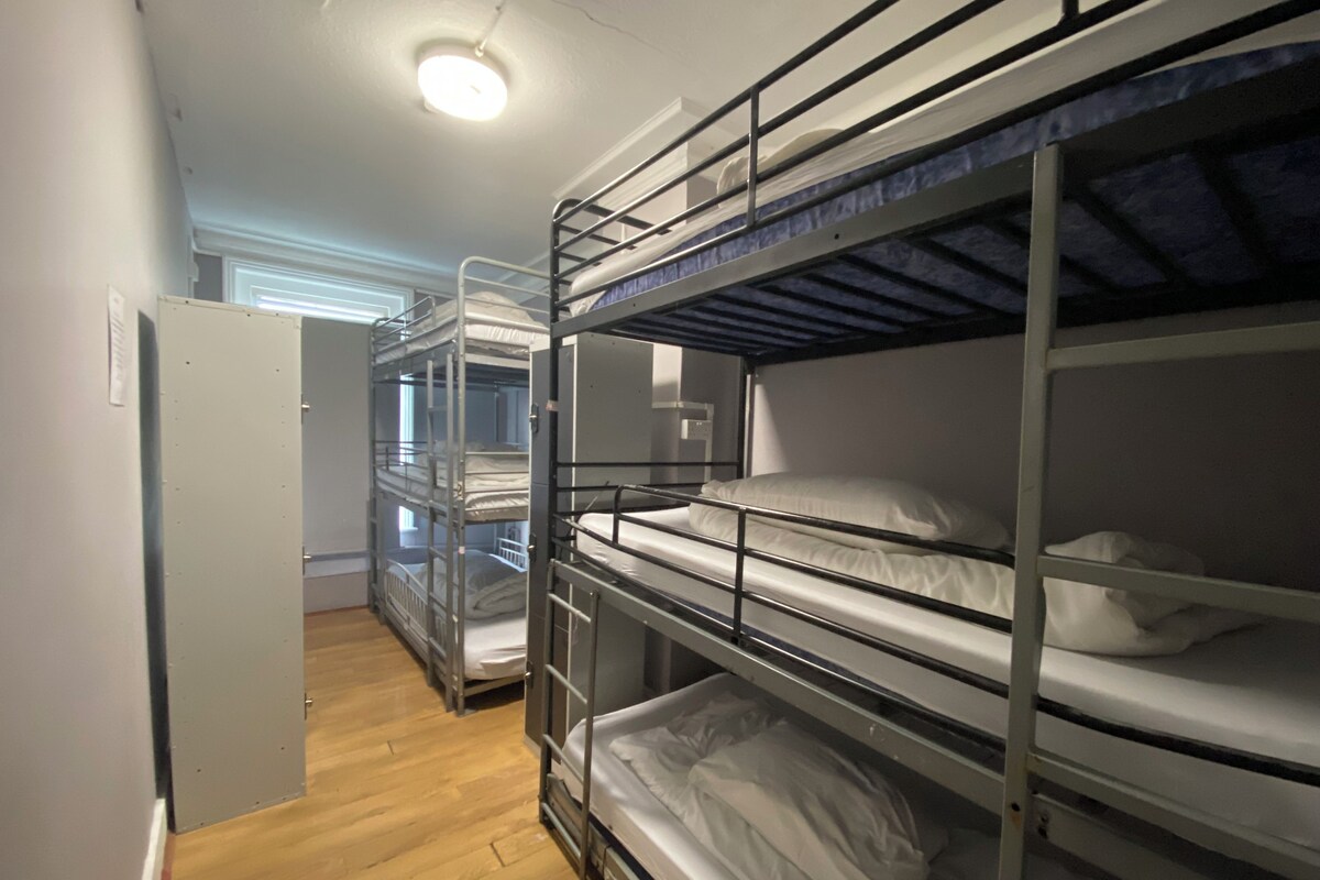 Une chambre avec des lits superposés, un plancher en bois et une porte située sur le côté gauche.