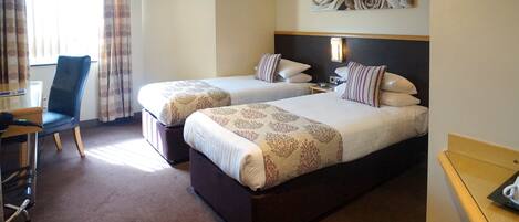A hotel room with two beds, a desk, a chair, and a large window with curtains.