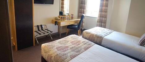 A hotel room with two beds, a desk with a chair, a TV, and a window with curtains.