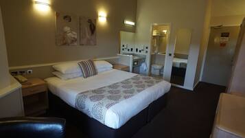 Une chambre d’hôtel comprenant un lit, des tables de chevet, un miroir, une salle de bain avec des toilettes et un lavabo, ainsi qu’une chaise.