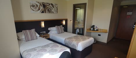 A hotel room with two beds, a small desk, a mirror, and a door.