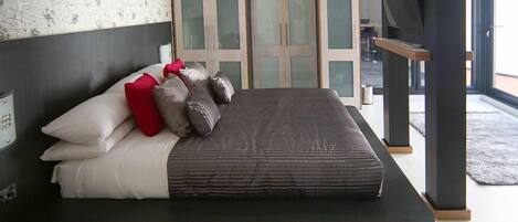 A modern bedroom with a bed, pillows, a TV, and a wardrobe.