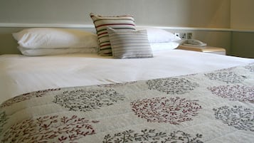 A neatly made bed with a floral-patterned bedspread, a striped pillow, and a plain pillow.