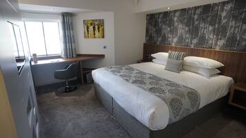 A modern hotel room with a large bed, a desk, and a chair.