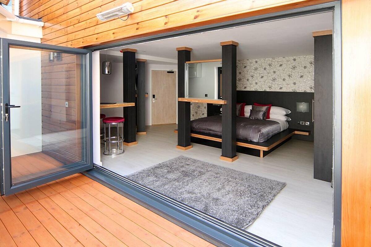 A modern bedroom with a bed, a small stool, and a sliding glass door leading to an outdoor area.