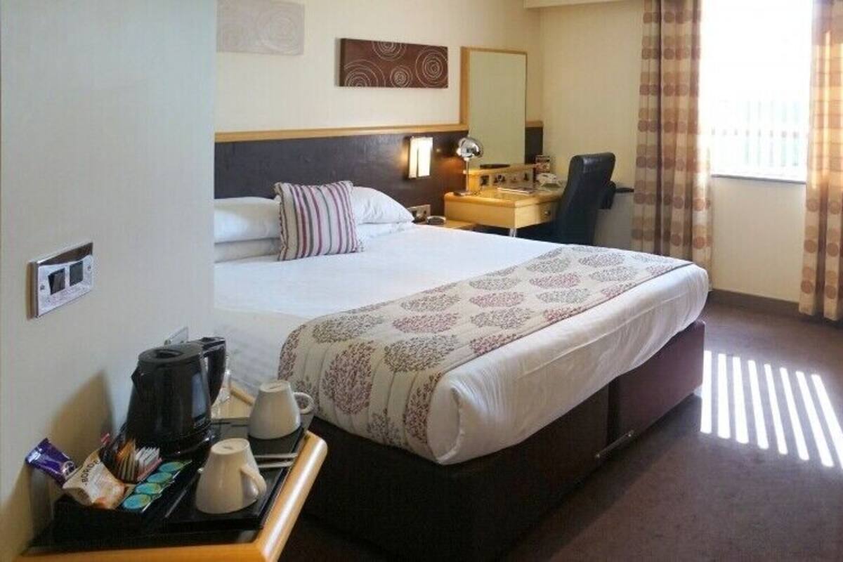 A hotel room with a large bed, a desk with a chair, a coffee maker, and a TV mounted on the wall.