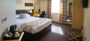 Una habitación de hotel con una cama grande, un escritorio con silla, cafetera y televisor montado en la pared.