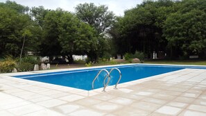 Ein rechteckiger Pool mit bepflastertem Rand, umgeben von Bäumen und einem parkenden Auto im Hintergrund.