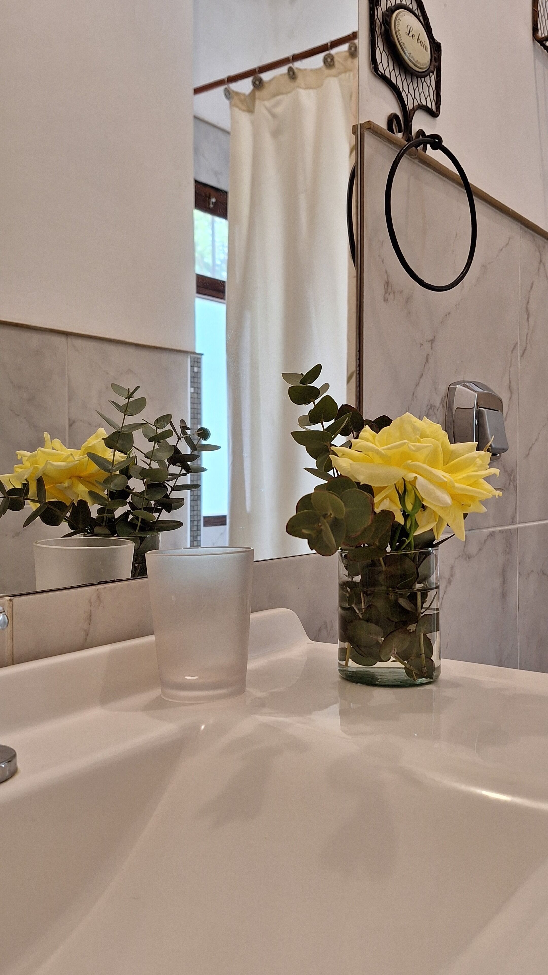 A bathroom with a mirror, a clock, and two vases with yellow flowers on the sink.
