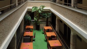 A multi-level indoor space with tables and chairs arranged on a green carpeted floor, surrounded by stone walls and a central plant. - Prixair Pure Hotel Wuse (Abuja)