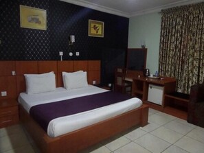 A hotel room with a large bed, a wooden headboard, a desk with a chair, a small cabinet, and a mirror. - Prixair Pure Hotel Wuse (Abuja)