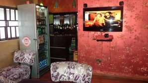 A bar area with a refrigerator stocked with beverages, a television mounted on the wall, and two patterned chairs. - Prixair Pure Hotel Wuse (Abuja)