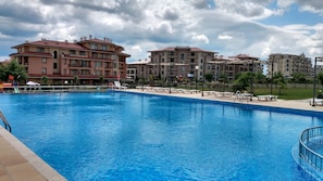 A swimming pool with lounge chairs and a view of multi-story buildings in the background.