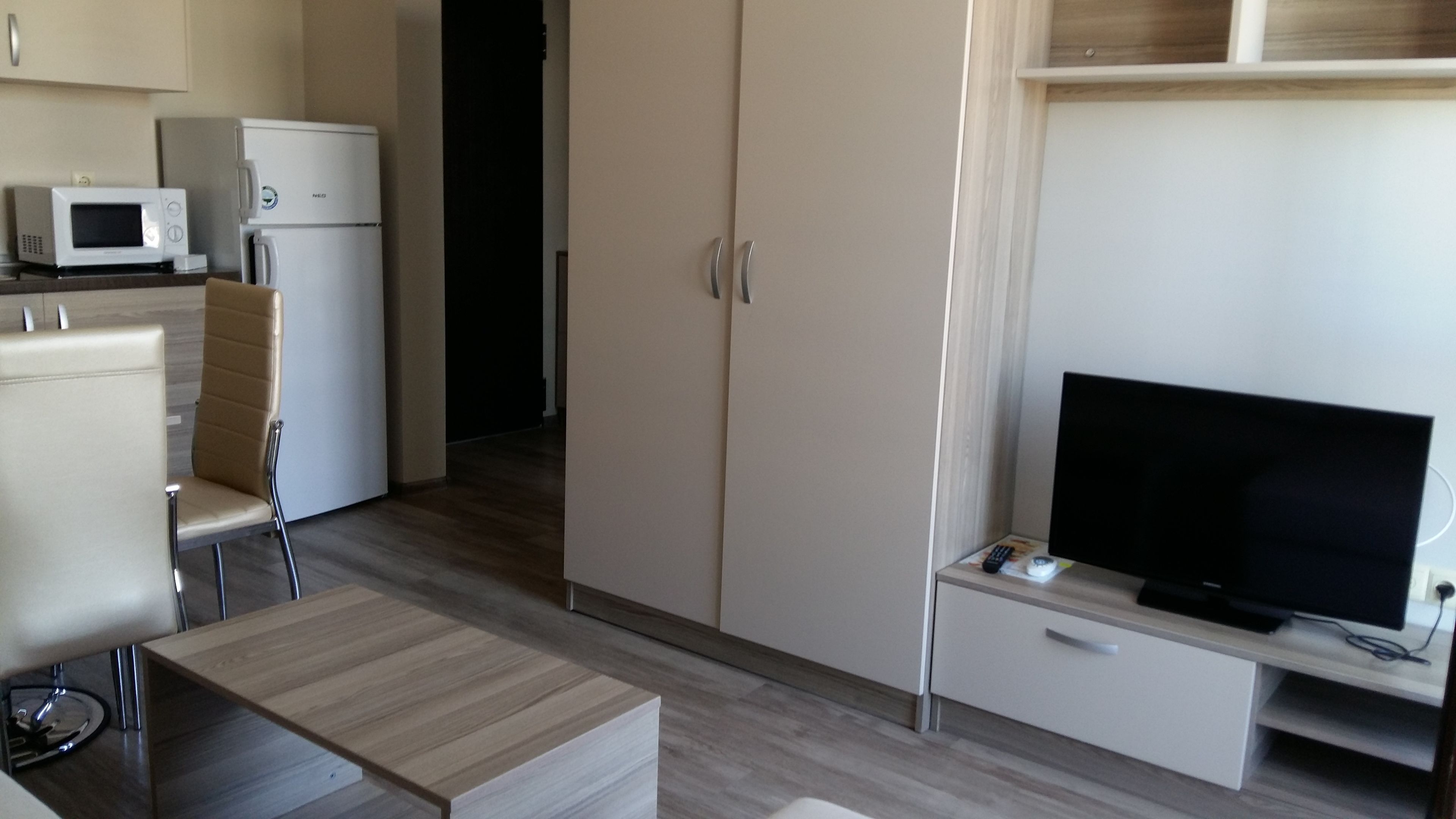 A compact hotel room with a kitchenette, a TV, a sofa, and a dining table.