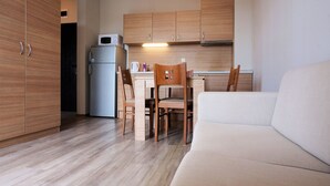 A compact kitchen with wooden cabinets, a refrigerator, a microwave, and a dining area with a chair and table.