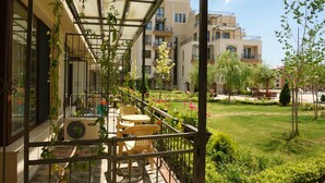 A balcony with outdoor seating, a garden, and a view of multi-story buildings.