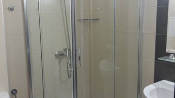 A glass-enclosed shower stall with a white sink and toilet visible in the adjacent room.