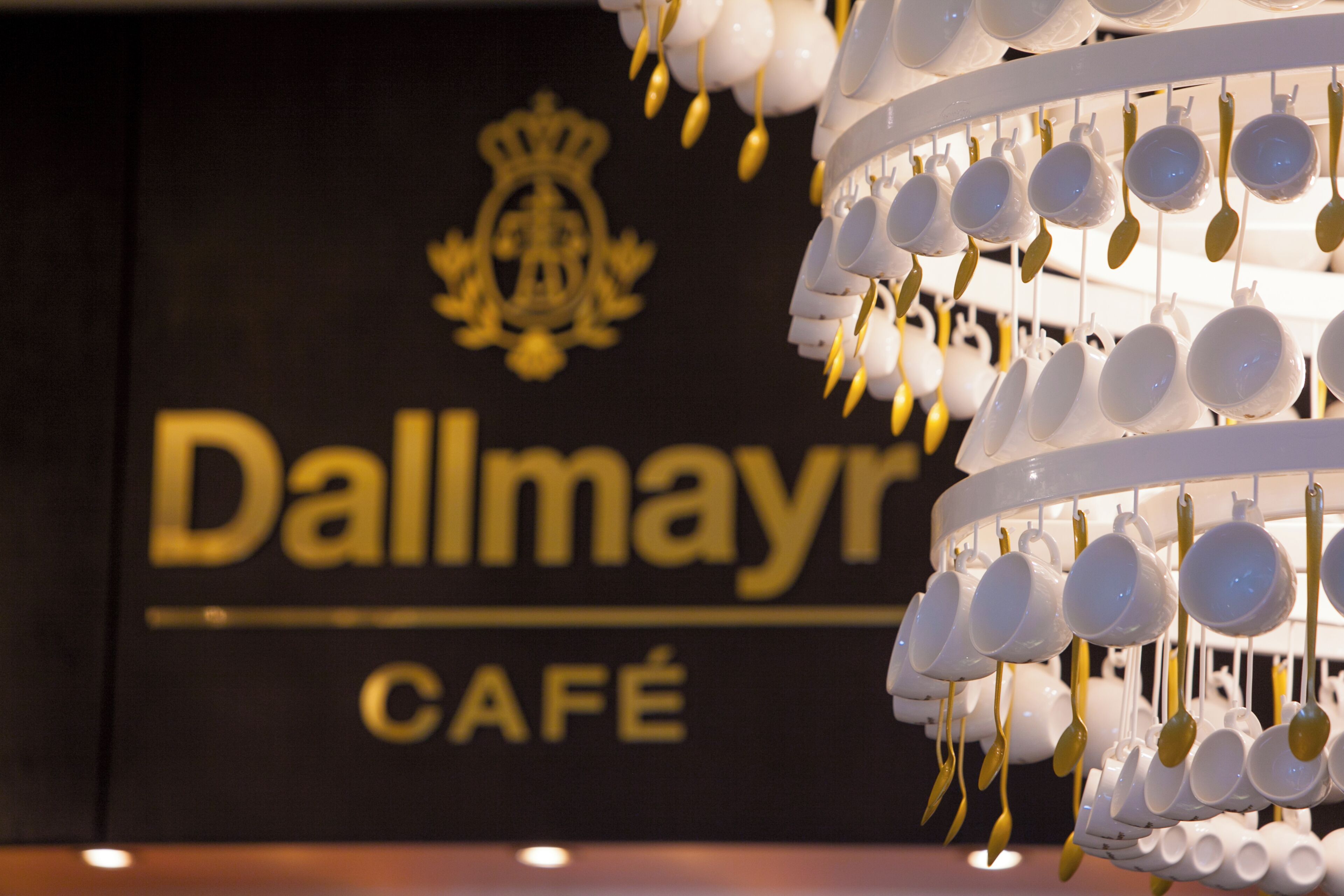 Una pared con el texto 'Dallmayr CAFÉ' y una composición decorativa de tazas y cucharas blancas.