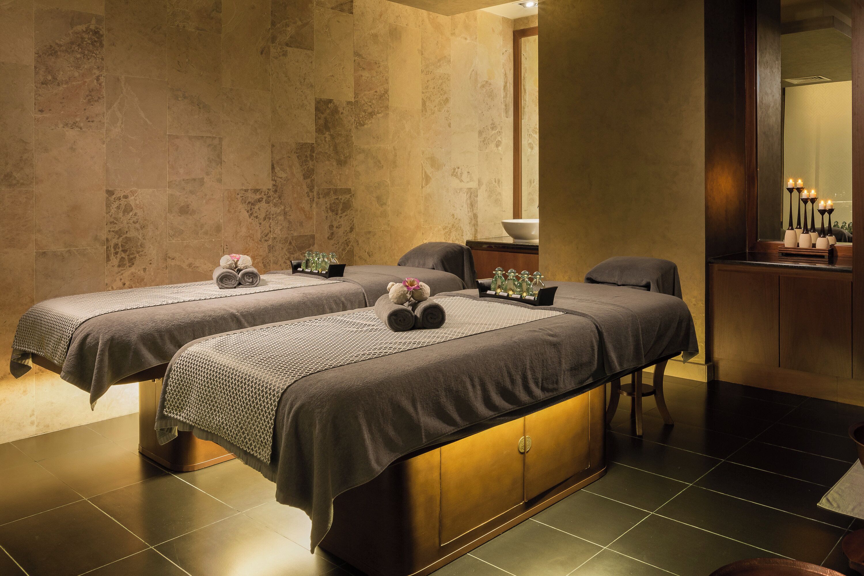 A spa room with two massage tables, a large mirror, and a small altar with candles.