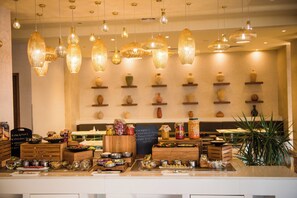 A restaurant interior with hanging light fixtures, a variety of dishes displayed on the counter, and shelves with decorative vases. - Grand Millennium Muscat connected to Muscat Grand Mall (Muscat)