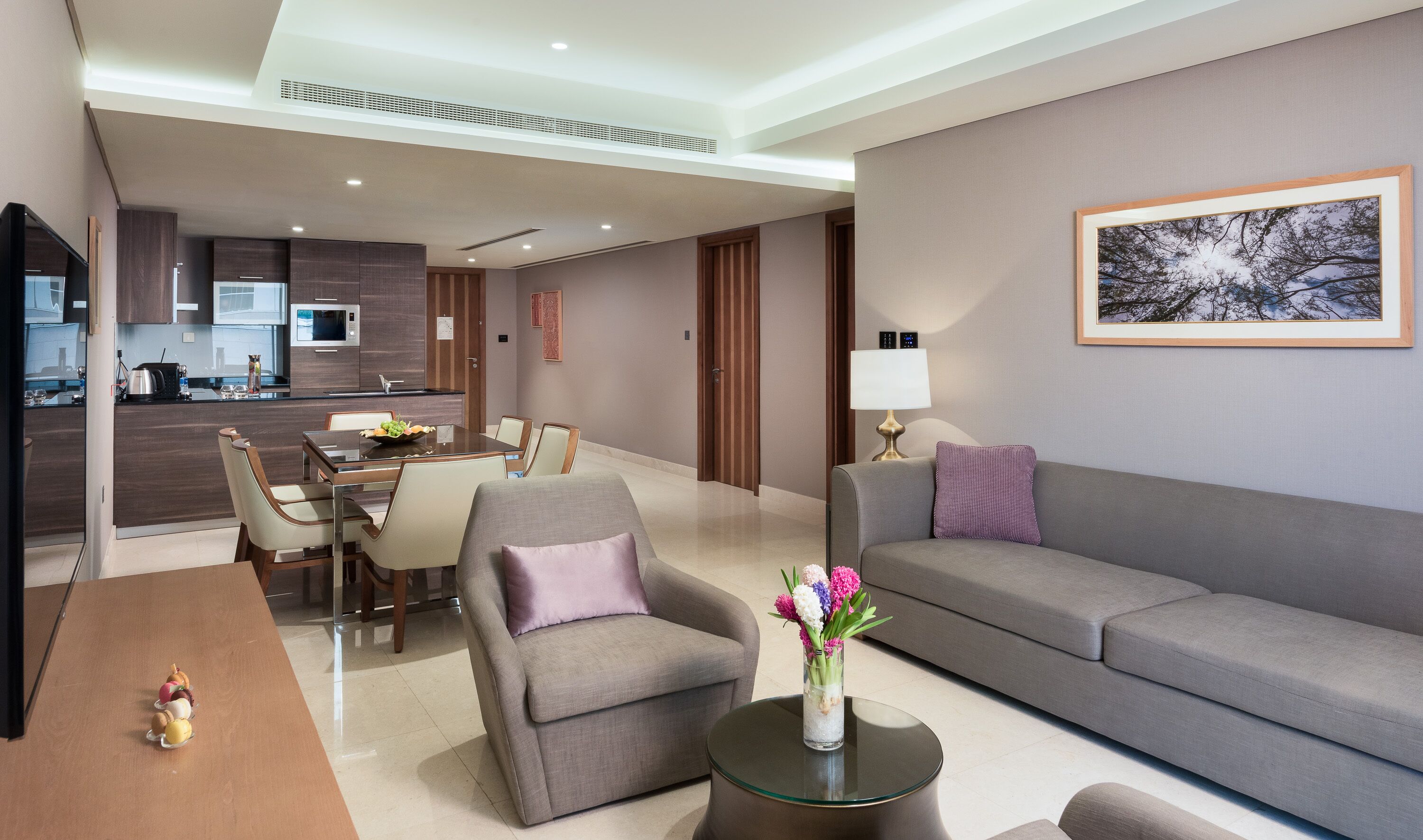 Una sala de estar moderna con un sofá gris, un comedor con mesa de vidrio, y una cocina al fondo.